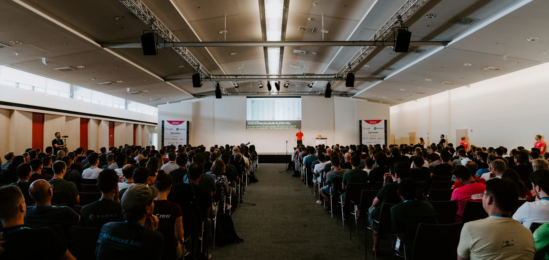 A full conference hall in daylight with delegates facing the stage
