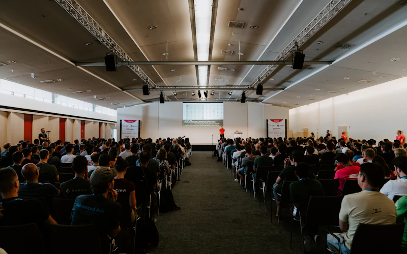 A full conference hall in daylight with delegates facing the stage