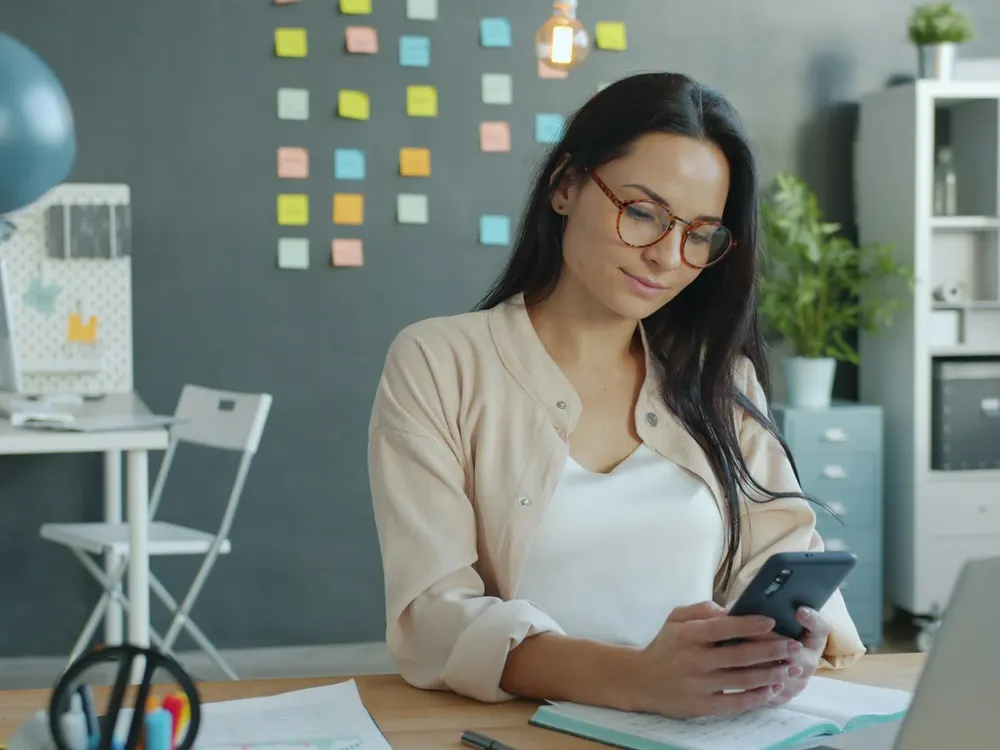 A smiling professional checking her phone at her desk
